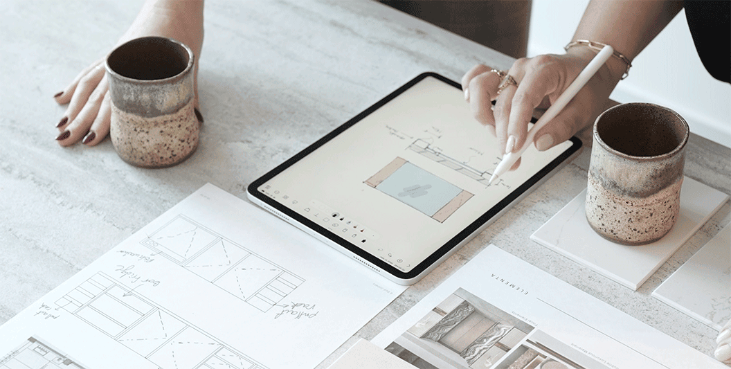 A pair of hands drawing a floor plan on a tablet with a white stylus.