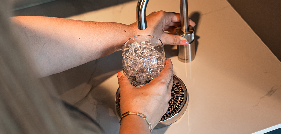 Person filling glass with ice cubes at a kitchen sink. Elementa Interior Design Dubai