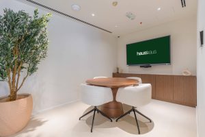 Modern conference room with a round wooden table, white chairs, and a large wall-mounted screen for.
