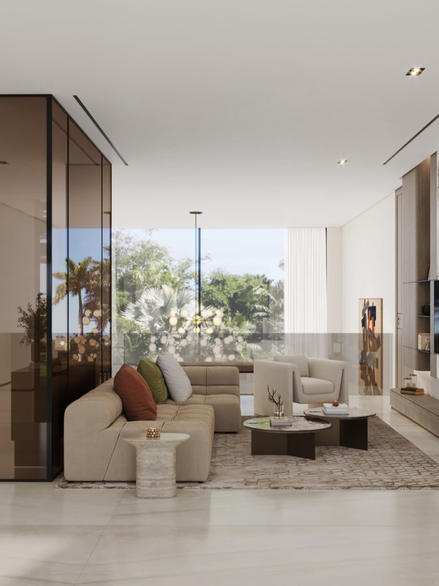 Living room with a low beige sofa, rust and olive cushions and round coffee tables beside a bronze glass column, with palm trees beyond the glass balustrade
